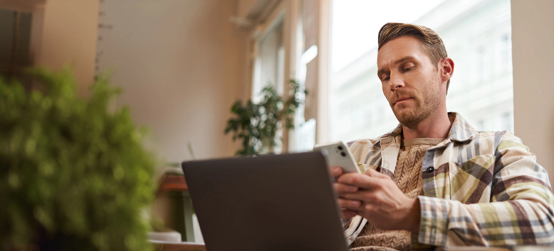 Man In Cafe With Laptop Looking At Smartphone