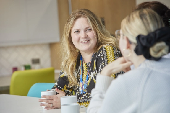 Two staff members in office kitchen chatting over a cup of tea