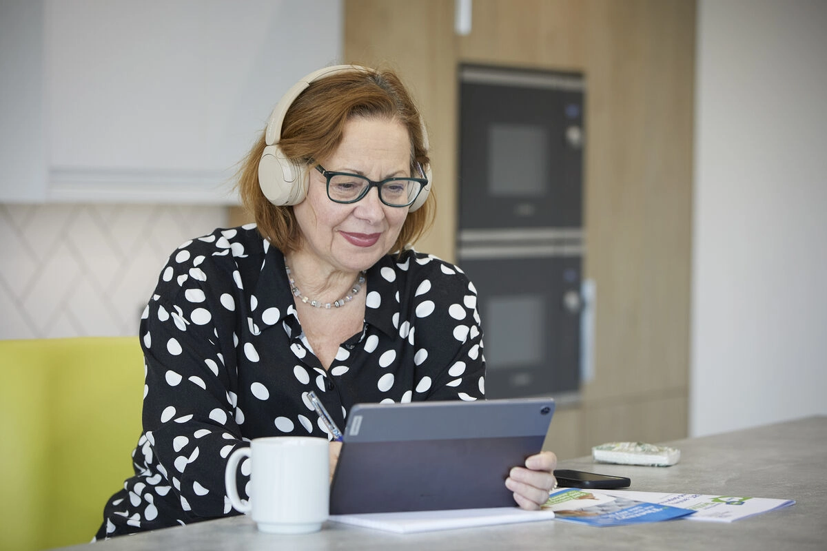 Woman wearing headphones Looking At Tablet In Kitchen