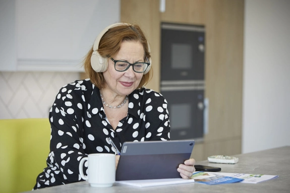 Woman wearing headphones Looking At Tablet In Kitchen